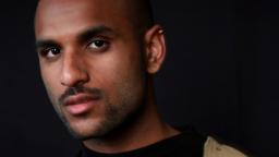 Head shot of person with shaved head, facial hair and wearing an earring.